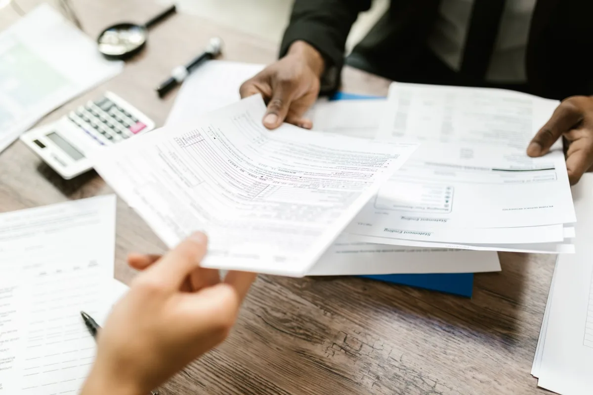 Two people exchanging paperwork across a desk with a calculator