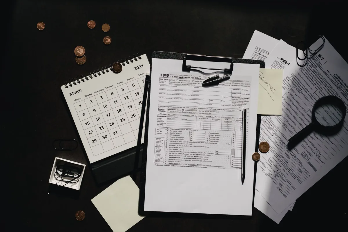 A clipboard with tax forms, a calendar and a calculator on a dark desk