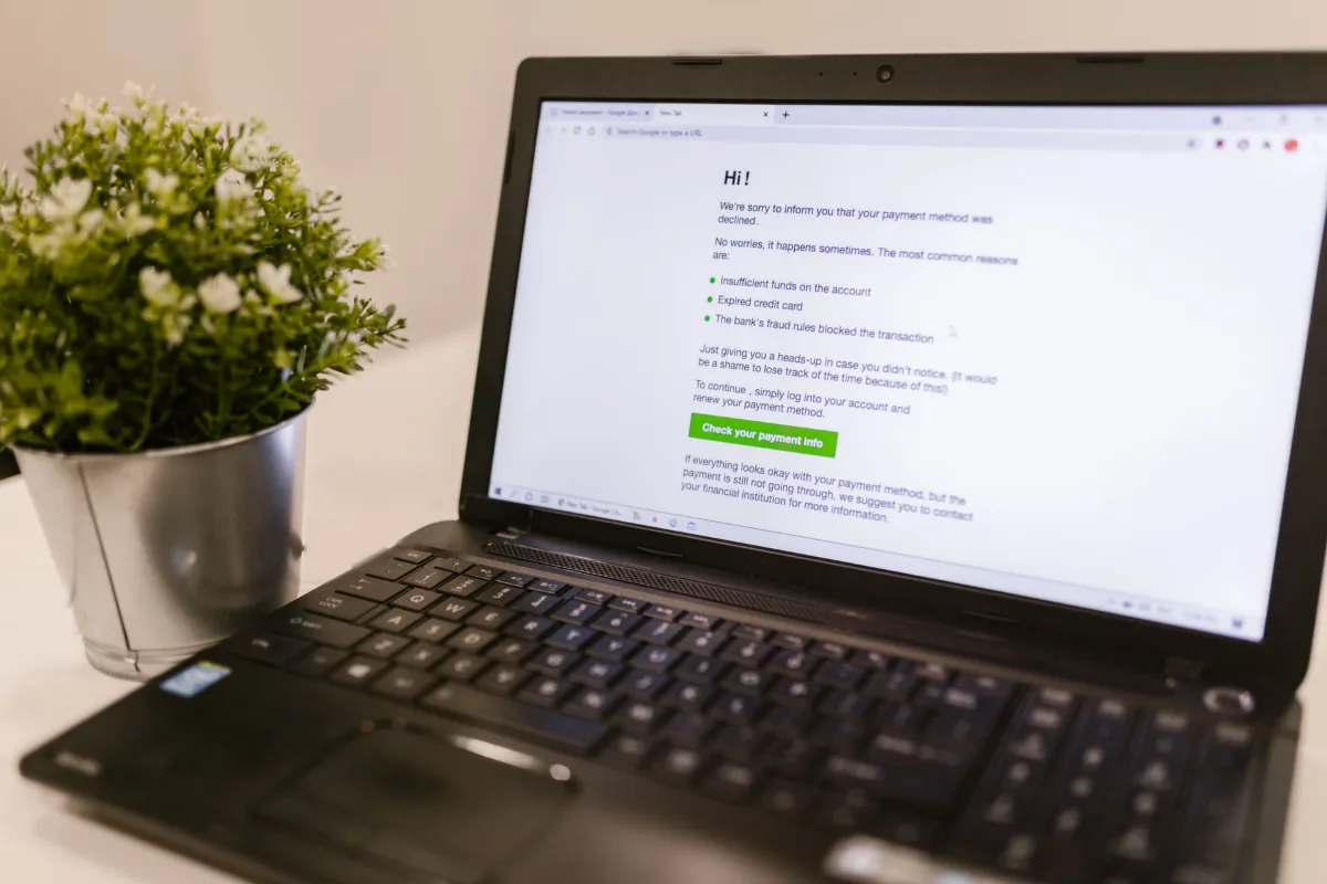 A laptop showing a payment notice on a table with a plant