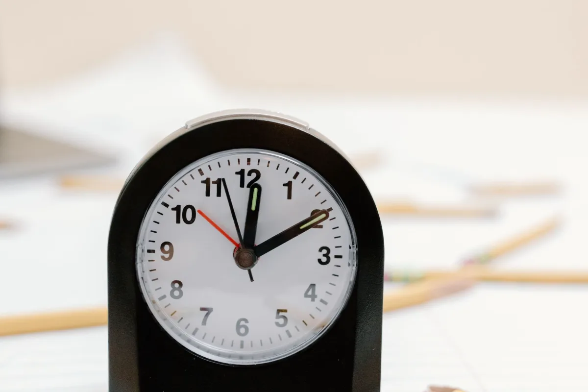 A clock on a desk among scattered pencils and papers