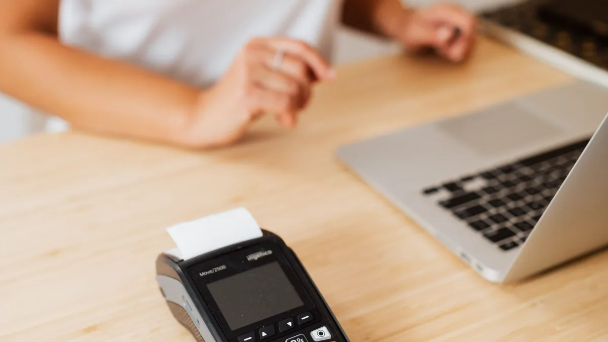 A card payment terminal on a wooden counter beside a laptop