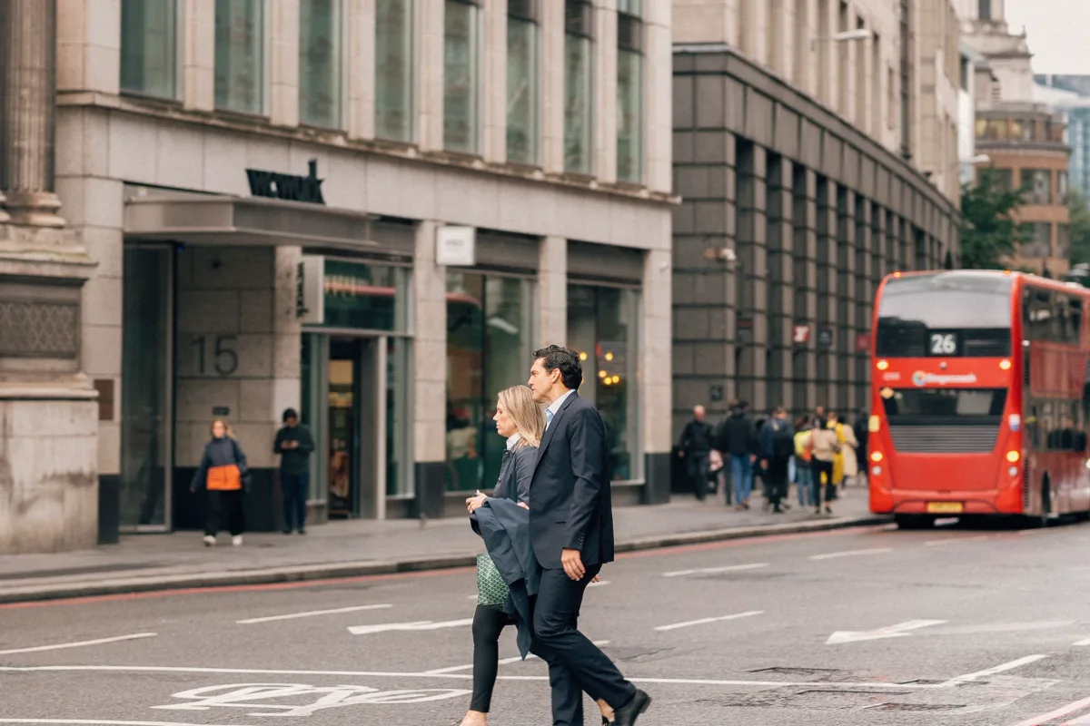 Pedestrians and a red bus on a busy street with office buildings