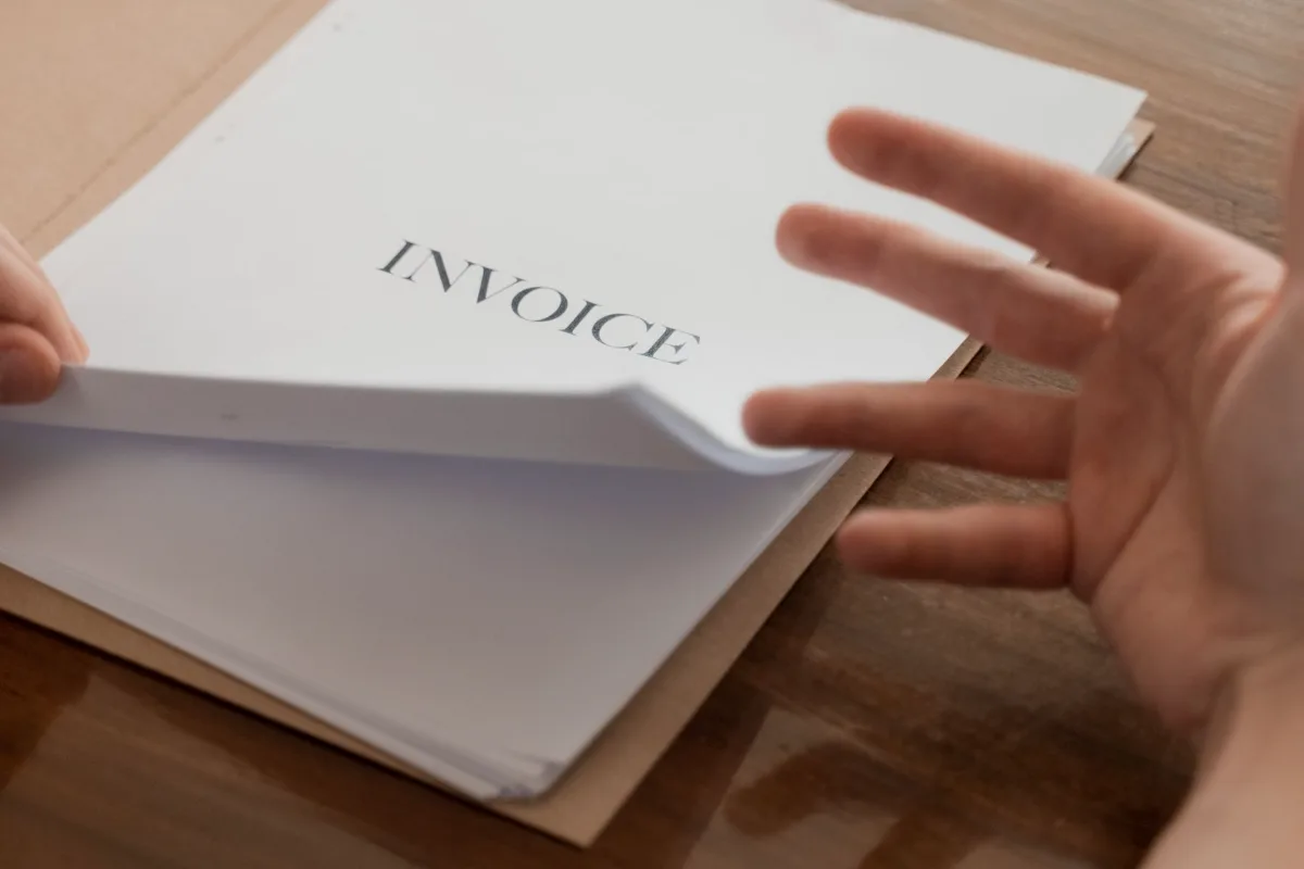 A stack of paper invoices on a desk being sorted by hand